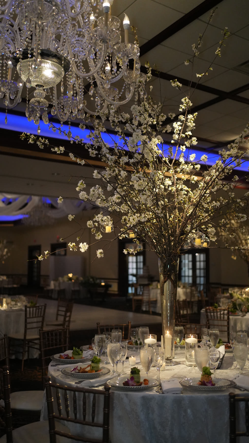 Grand Ballroom table set beneath a chandelier with tall white blossom centerpieces