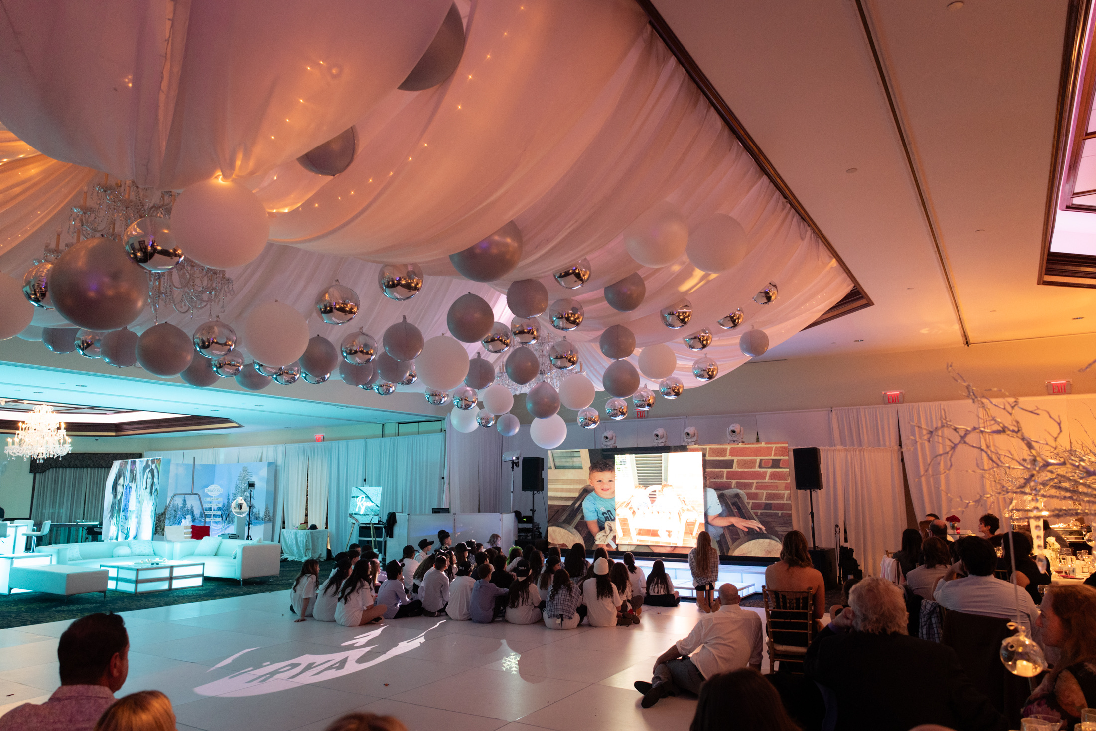 Grand Ballroom transformed with ceiling drapery, suspended balloons, lounge seating, and a large video screen