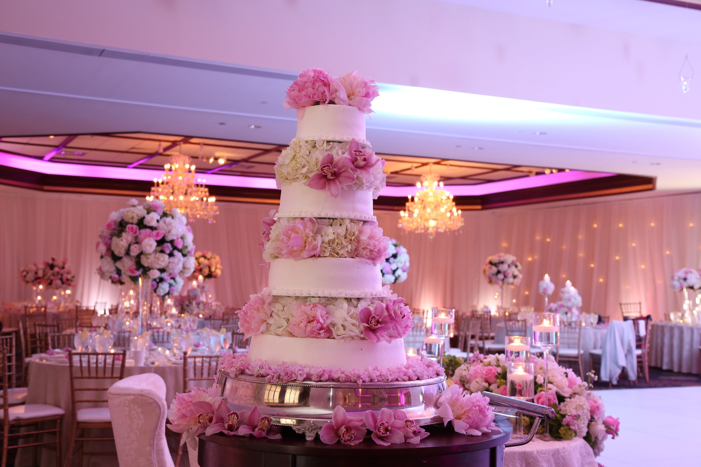 Pink and white floral tiered cake displayed in the decorated ballroom