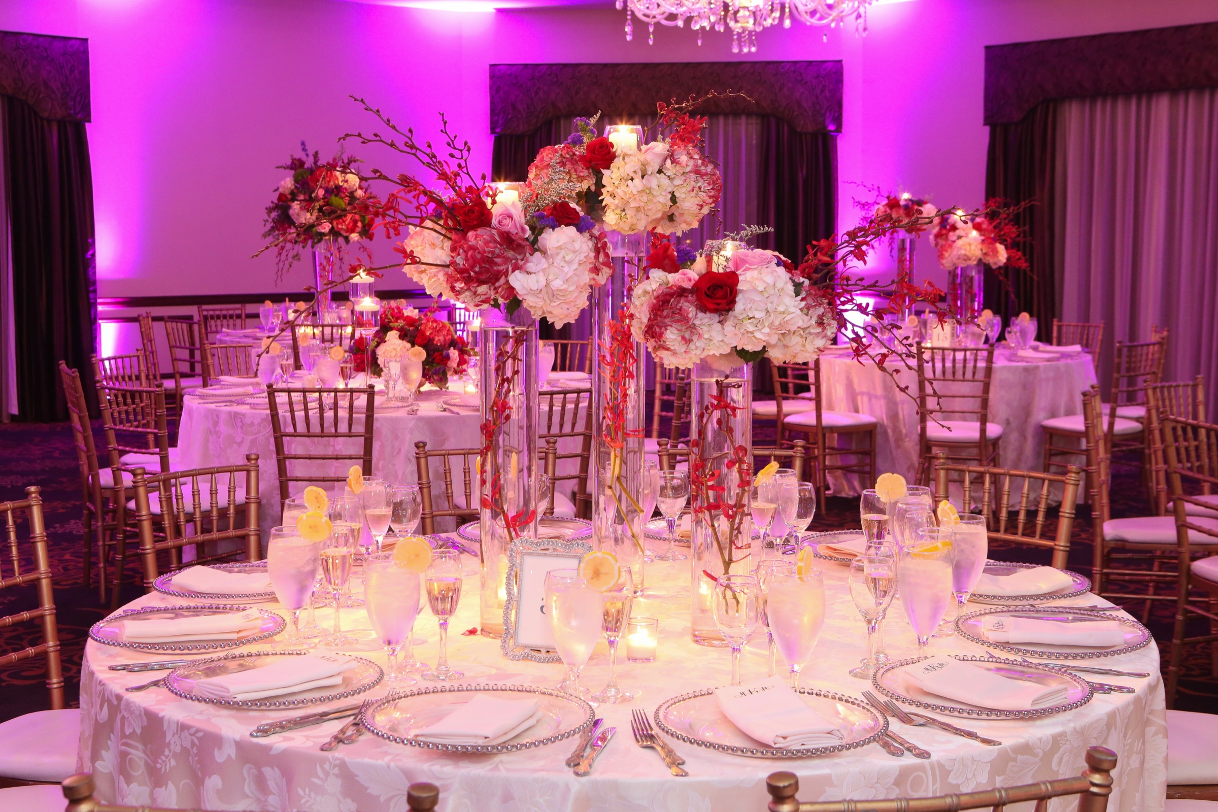 Red, pink, and white floral centerpiece in the ballroom beneath vivid uplighting
