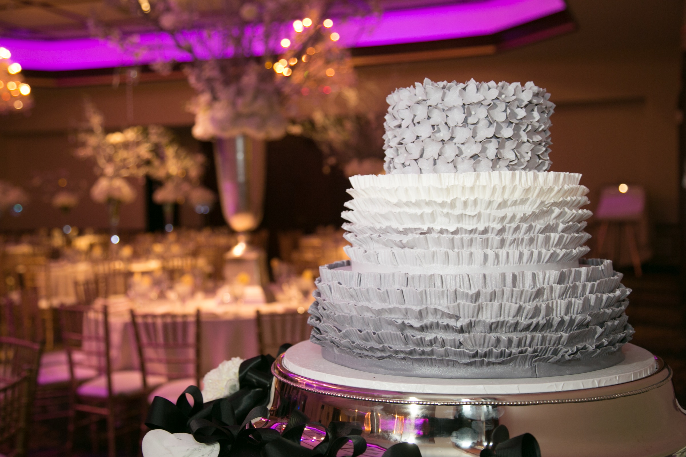 White tiered cake displayed in the ballroom beneath purple uplighting