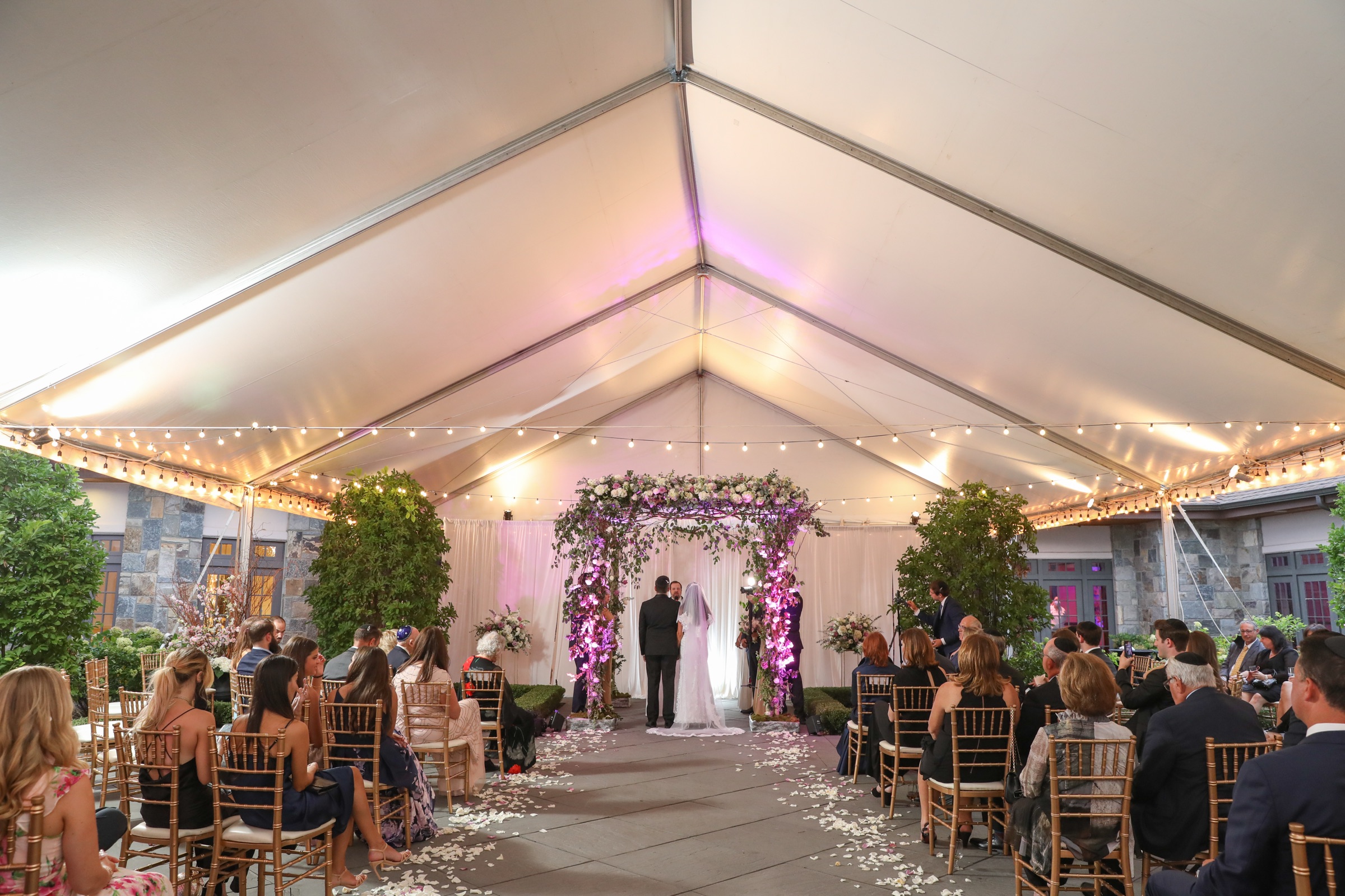 Wedding ceremony beneath a flower-lined chuppah in the outdoor courtyard