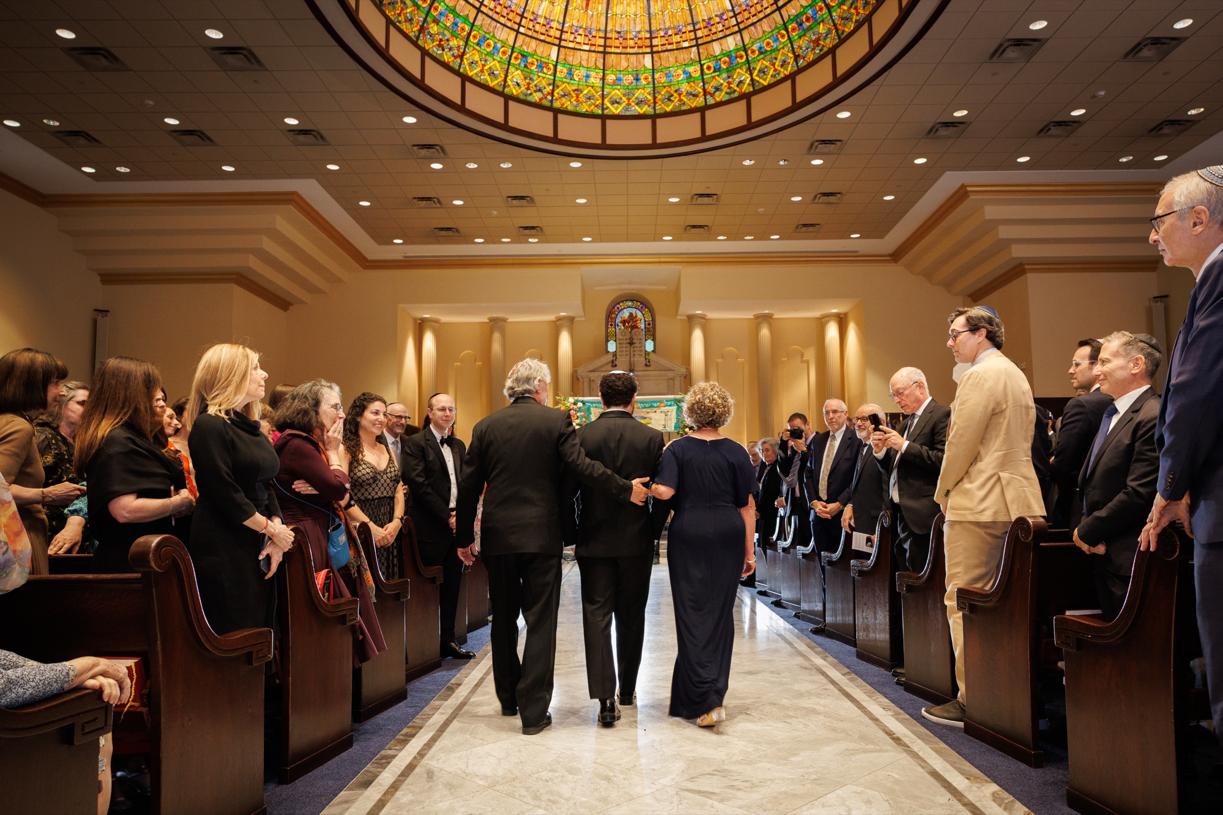 Groom walking down the sanctuary aisle with his parents during the processional
