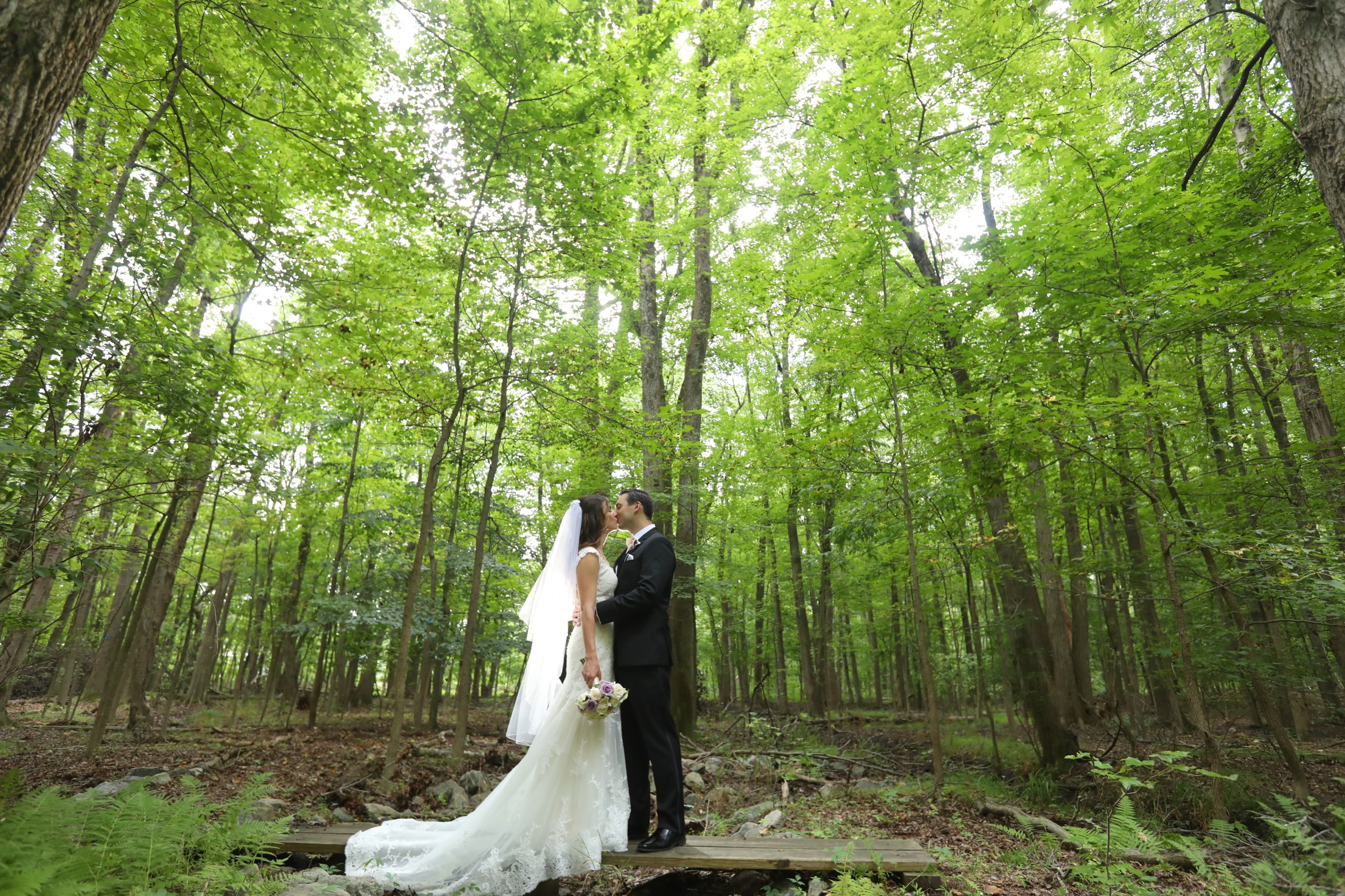 Newlyweds sharing a kiss among the wooded grounds