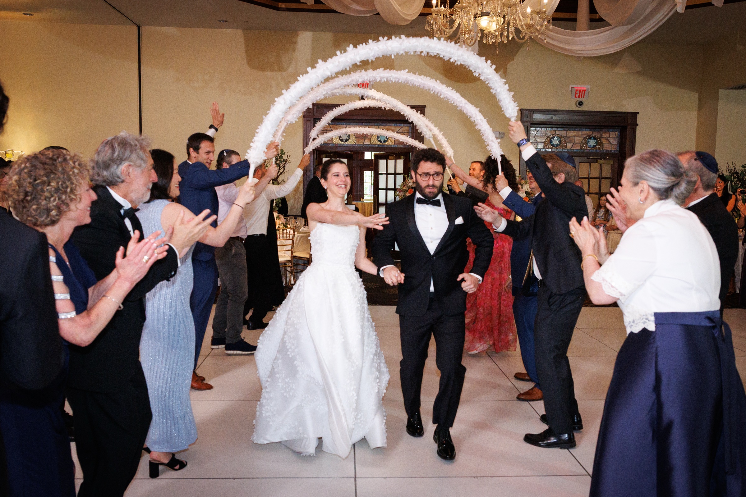 Newlyweds entering their reception beneath a celebratory arch of feathers